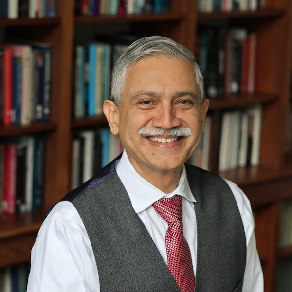 Adnan Hyder in vest and red tie with bookshelf background